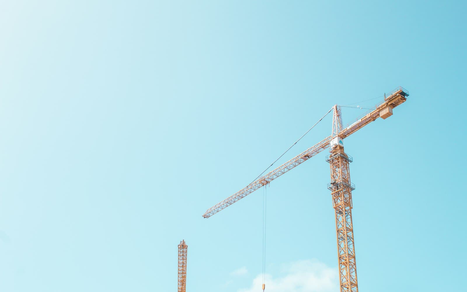 Stock photo of yellow tower cranes against a clear blue sky at a construction site