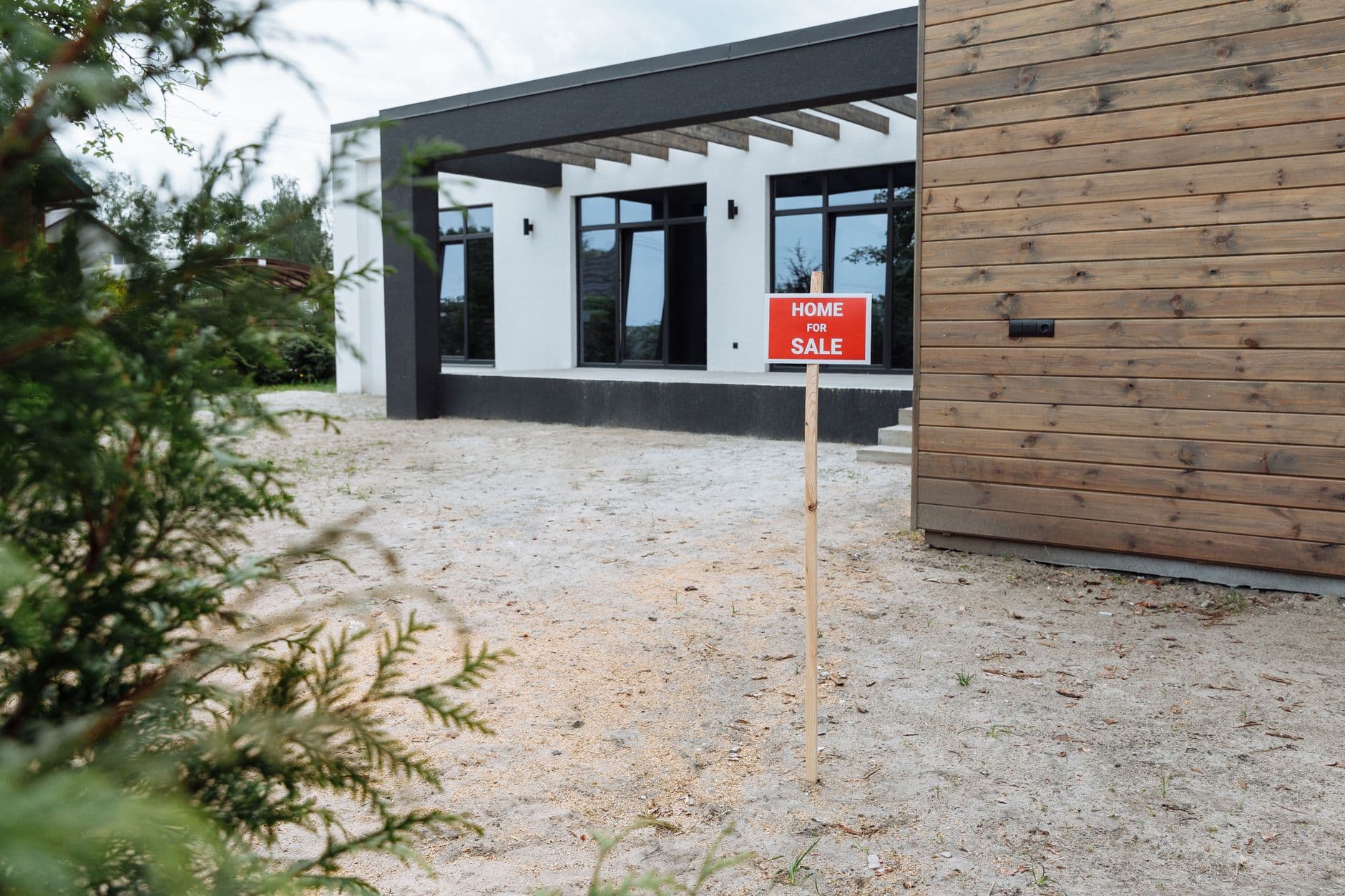 Stock photo of a modern house with a red “Home For Sale” sign in the front yard